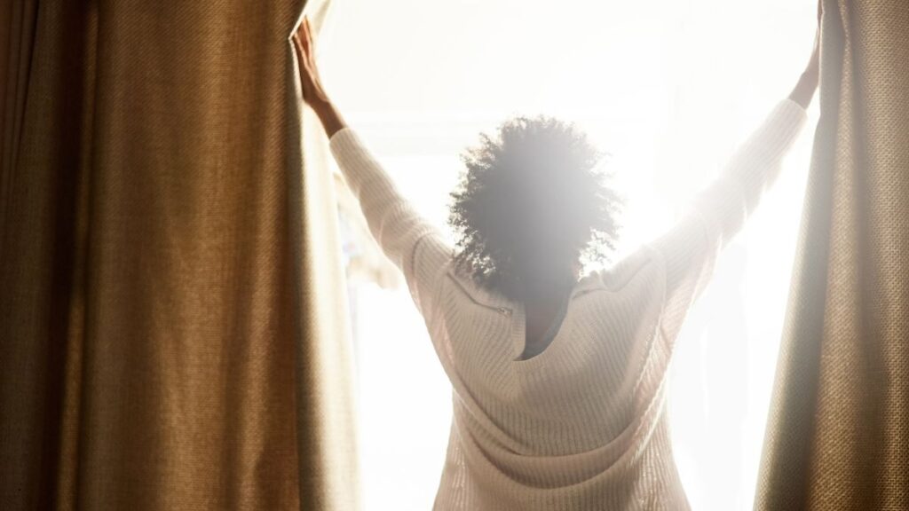 Person opening curtains to morning light – blog post about chronic illness and self-worth.
