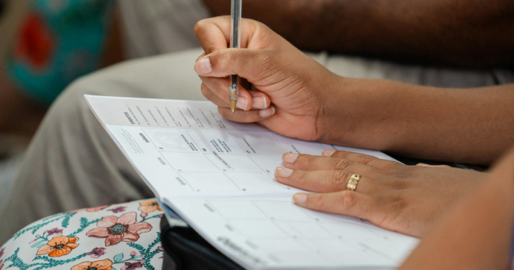 Person writing goals on a weekly planner calendar for goal follow through